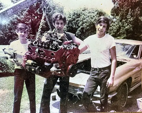 Bill, Harry and Steve Moppert lifting a V8 engine on a chain hoist, 1972
